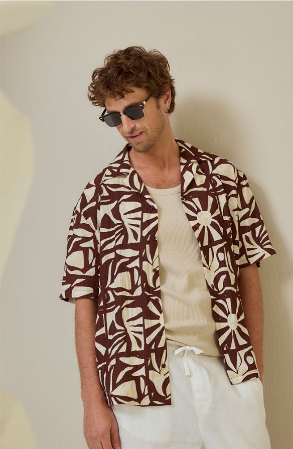 Man in a brown and cream abstract-print shirt, ribbed vest and white linen trousers